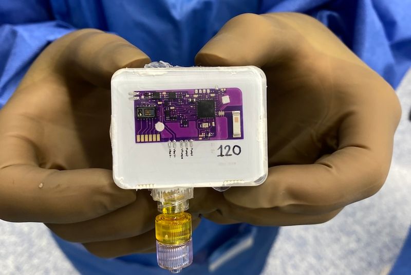 close up of Naloximeter implantable device, a white rectangle with a purple chip, being held in gloved hands