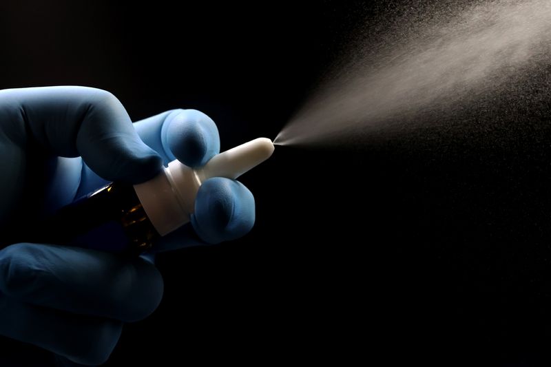 blue-gloved hand operating nasal spray against a black background