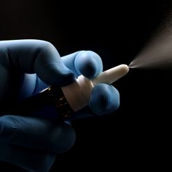 blue-gloved hand operating nasal spray against a black background