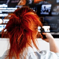 A woman with red hair holds a TV remote watching Netflix on big screen. 