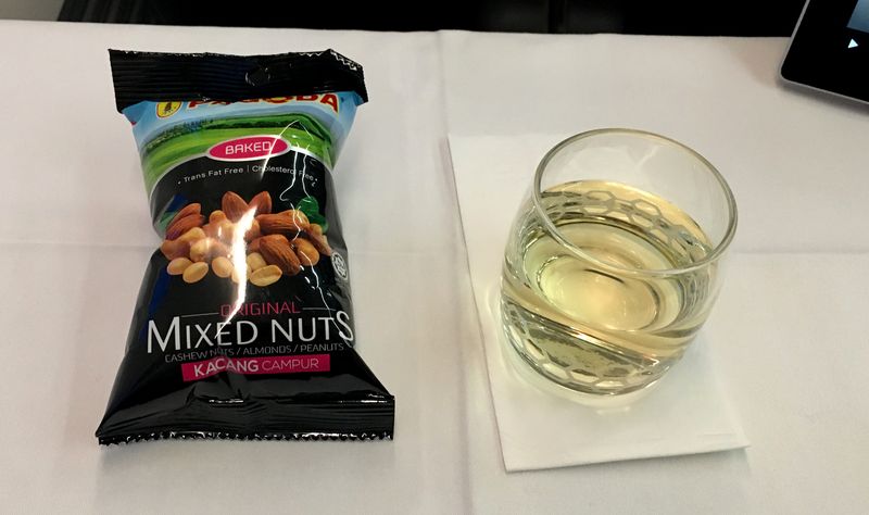 airplane tray table with a bag of mixed nuts and a tumbler of white wine