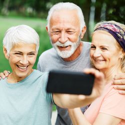 three senior people, two women and one man, smiling together and taking a selfie in a park, wearing exercise clothes