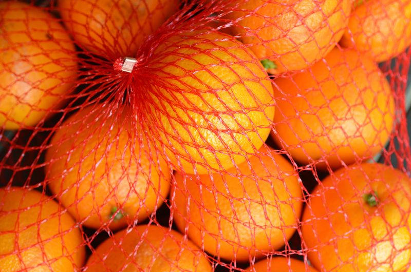 Fresh oranges fruit in a red plastic netting bag.  