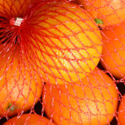 Fresh oranges fruit in a red plastic netting bag.  