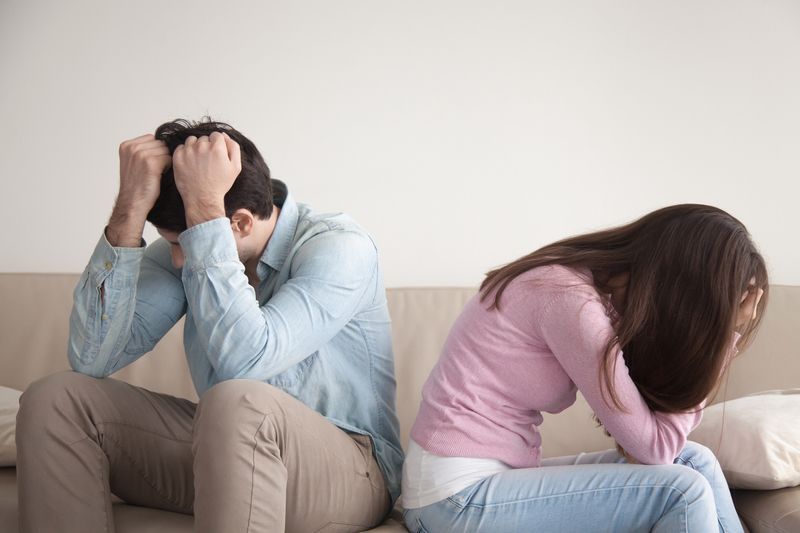 man and woman sat on sofa, turning away in visible pain