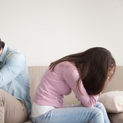 man and woman sat on sofa, turning away in visible pain