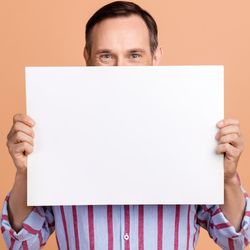 Photo of person holding large piece of blank paper in front of their face, against an orange background