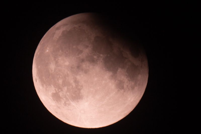 A photo of the full moon in the sky with a top right chunk covered by shadow due to Earth being in front of the Sun during a partial lunar eclipse 