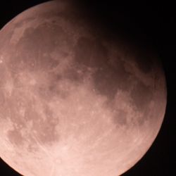 A photo of the full moon in the sky with a top right chunk covered by shadow due to Earth being in front of the Sun during a partial lunar eclipse 