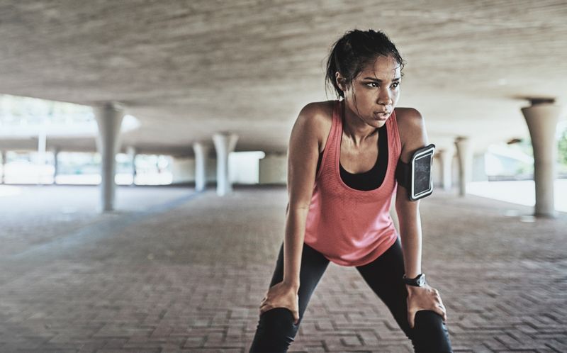 Person in pink tank top and phone strapped to their arm, resting after exercise while looking sweaty