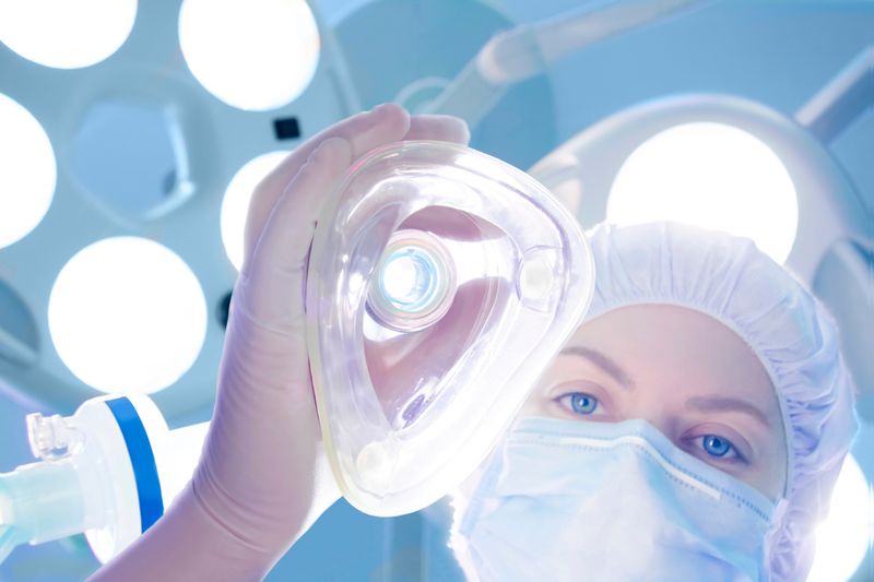 person in surgical cap and mask lowering a surgical gas mask down towards the camera