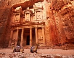 A photo taken from a low angle looking up at the entrance to the Treasury building. The photo shows the pillars and decorations carved into the canon's face. Two camels are seated in front of the entrance.