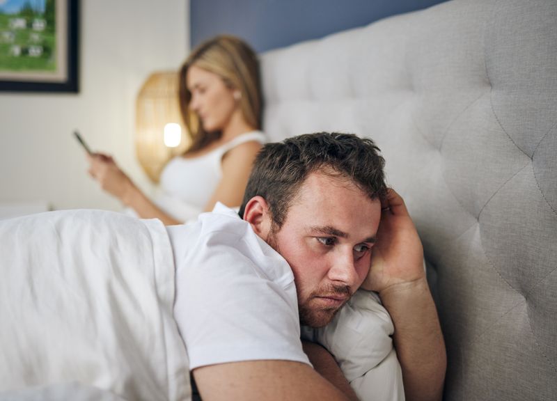 Shot of a young woman using a cellphone in bed after an argument with her husband.