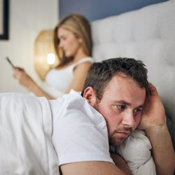 Shot of a young woman using a cellphone in bed after an argument with her husband.