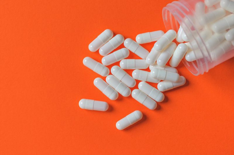 unlabelled bottle of blank, white capsules spilling out onto an orange surface