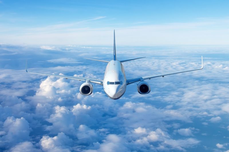 Passenger civil airplane jet flying at flight level high in the sky above the clouds and blue sky. View directly in front