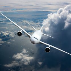 White passenger jet plane in the sky. Aircraft flying high above the cumulus clouds and ocean waves. Airplane front view and right roll.