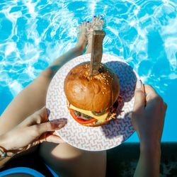 Top view of juicy Burger in girl's hands and feet in the pool. 