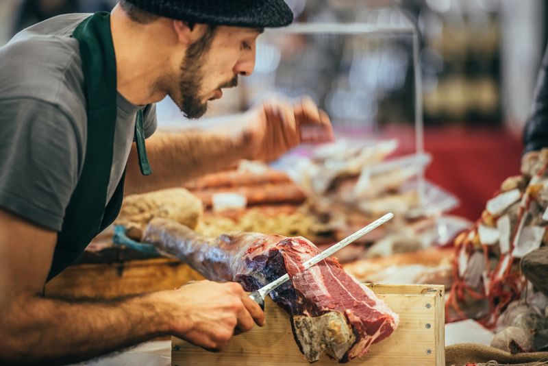 butcher slicing italian dry-cured ham prosciutto at food market in Genoa, Italy