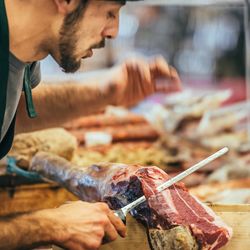 butcher slicing italian dry-cured ham prosciutto at food market in Genoa, Italy