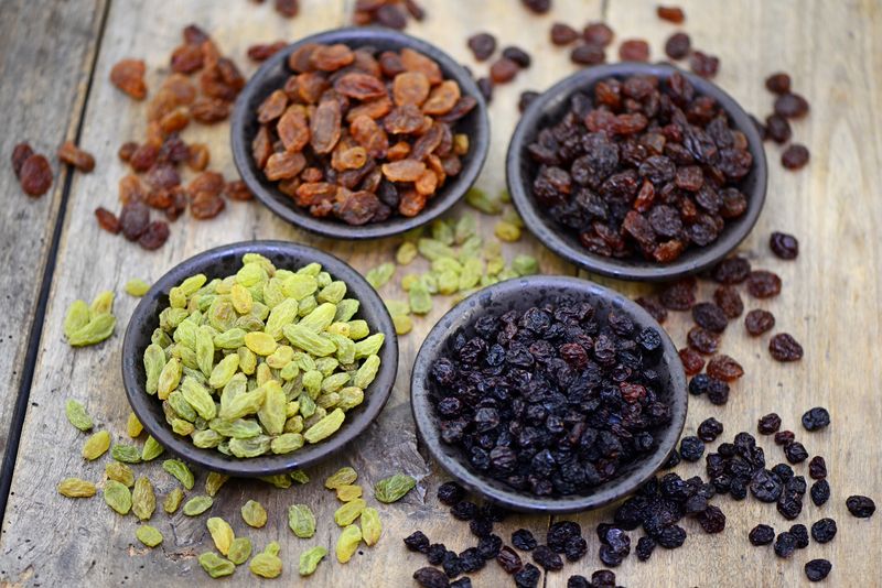 4 bowls of raisins, sultanas and currants of varying colors on a wooden surface