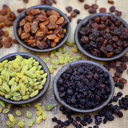 4 bowls of raisins, sultanas and currants of varying colors on a wooden surface