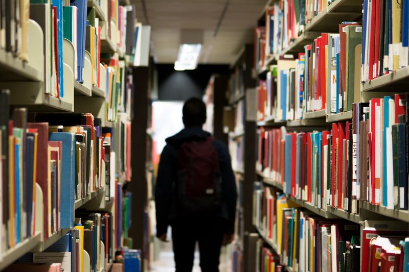 Person's silloute down an aisle of a library reading books.