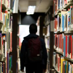 Person's silloute down an aisle of a library reading books.