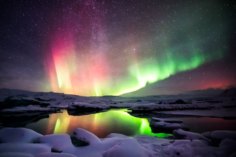 Red and green aurora in a starry sky above icy waters