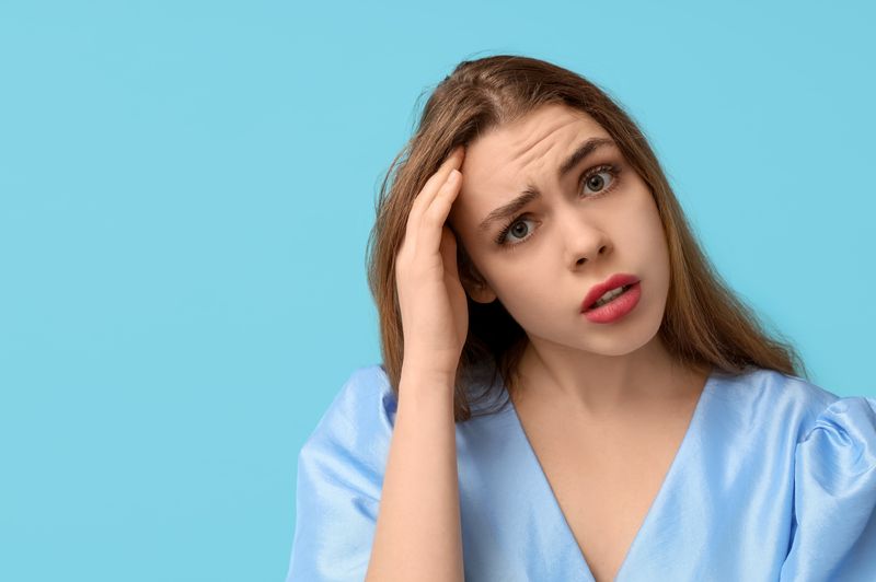 Thoughtful young woman trying to remember something on blue background.