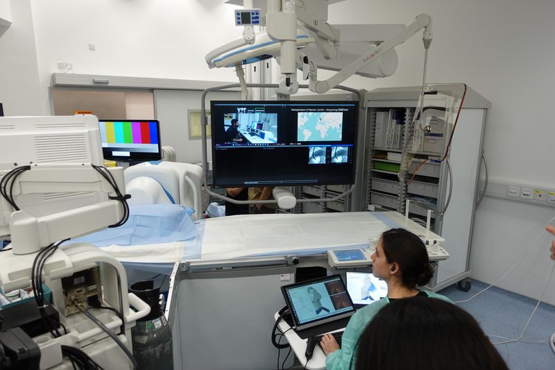 operating room in Hong Kong with scientist sitting at laptop; there's a big screen with an uplink to the other scientific team in Zurich