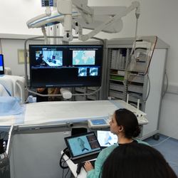 operating room in Hong Kong with scientist sitting at laptop; there's a big screen with an uplink to the other scientific team in Zurich