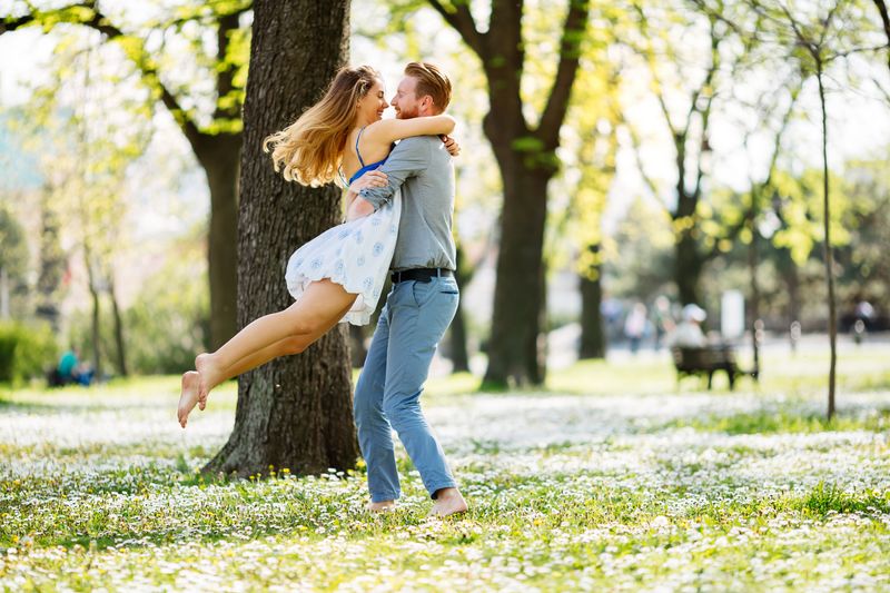 man lifts and swings around woman in park on sunny day