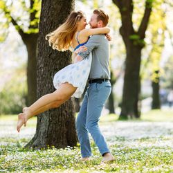 man lifts and swings around woman in park on sunny day