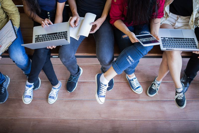 view from above of young people sat on a bench, some holding laptops and notebooks