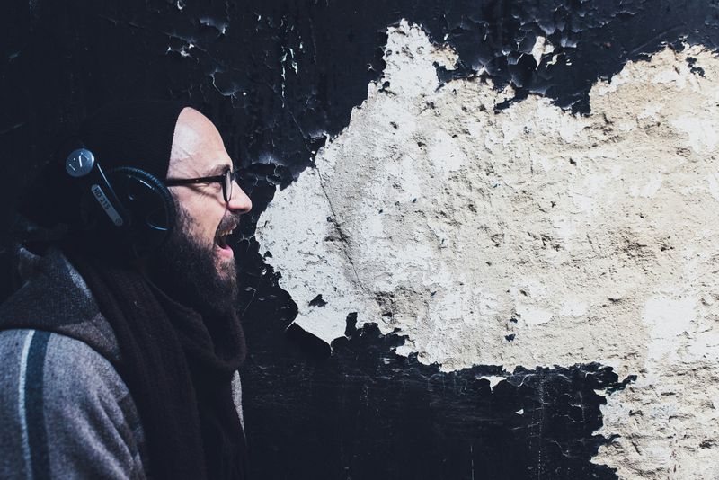 A man shouting and talking against the backdrop of a black old wall.