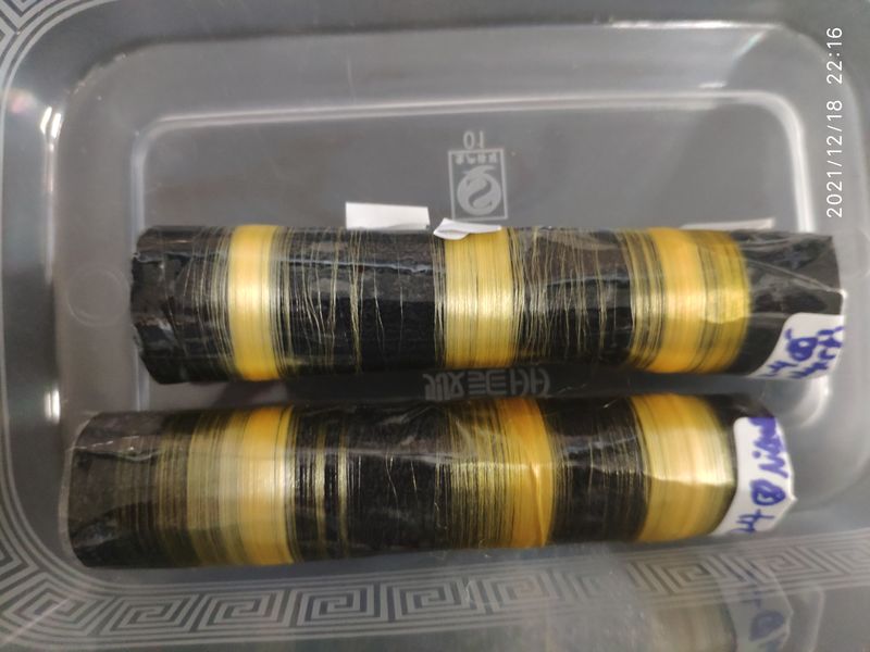 Strands of silk fibers made by the silkworms wrapped around black cylinders in a plastic box.