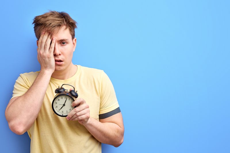 Sleep-deprived man holding alarm clock