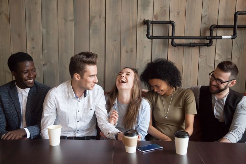 Young group of people chatting and laughing, sat in a cafe.