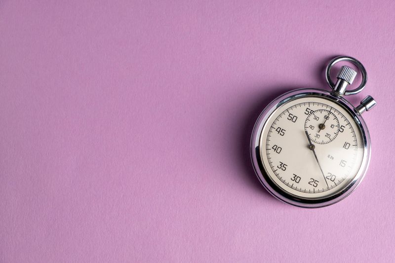 silver analog stopwatch on a lilac background