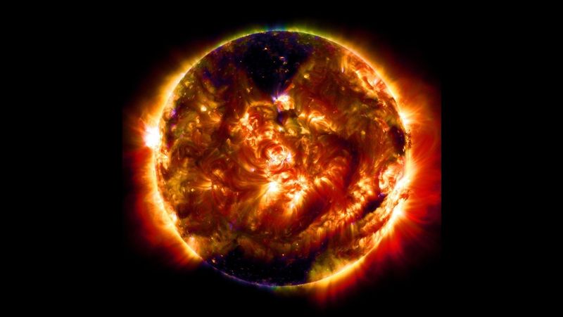  A mosaic image of the Sun in different wavelengths shows the swirling surface of the Sun in yellow, red, orange, and purple. Some areas of the star appear black, while light dances off the its atmosphere.