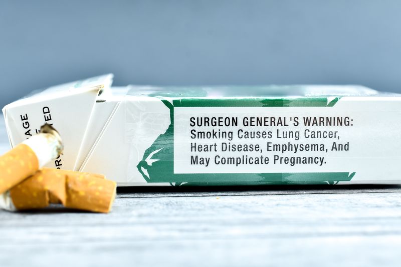 cigarette stubbed out next to packet of cigarettes with surgeon general's warning label about health risks clearly visible