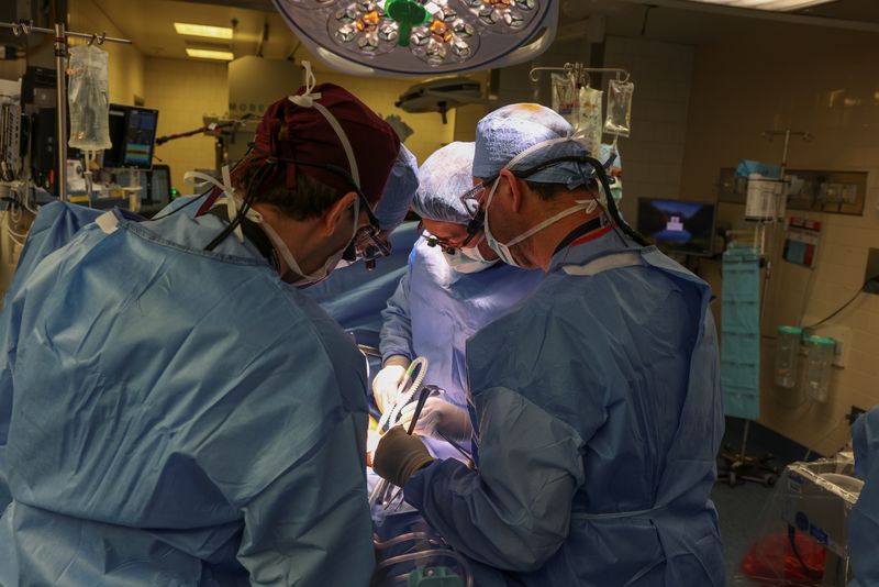 four surgeons working on the patient during the procedure; they're all wearing blue surgical gowns, caps and face masks