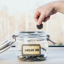 hand placing Euro coin in a glass jar labelled "Swear Jar"