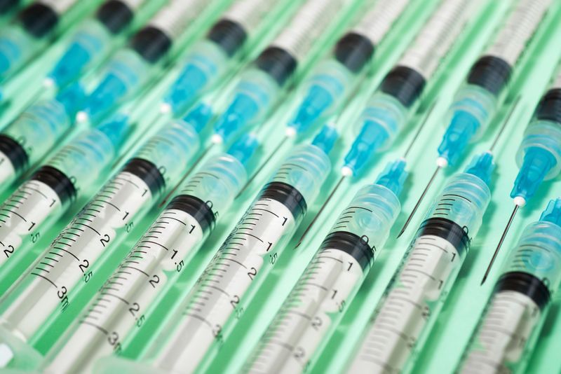 close-up of two rows of medical syringes lined up on a light green surface