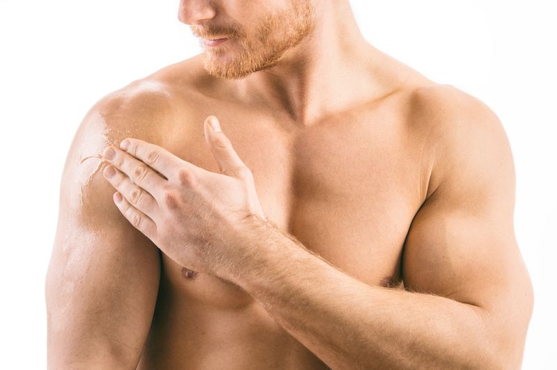 man pictured topless from waist up and eyes down rubbing clear gel onto shoulder