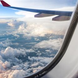 An photo take from a plane window. The shot shows an accumulation of clouds below the plane that look like bubbly mountains. The plane's left wing is visible in the top right of the photo.  