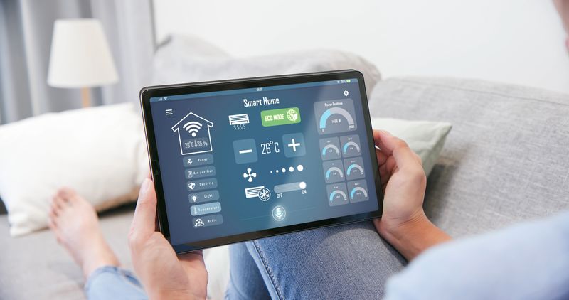 Person sat on sofa holding a thermostat tablet