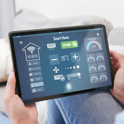 Person sat on sofa holding a thermostat tablet