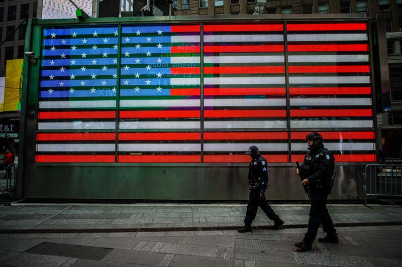 Two police officer men walking in front of an electronic USA flag in Time Square, New York, US